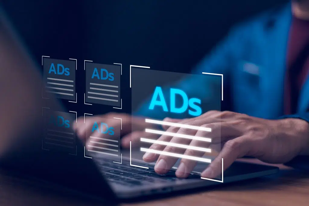 Hände an einer Laptop-Tastatur, davor schwebende Anzeigenflächen mit der Aufschrift ADs, Symbolbild für Klickbetrug bei Google Ads